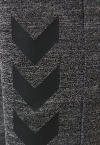 Grau texturierter Stoff mit schwarzen Chevron-Musterakzenten. Nahaufnahme des Materials und der Designdetails bei Sportbekleidung.