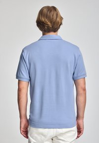 Ljusblå polo t-shirt i mjukt tyg, med klassisk krage, korta ärmar och rak fåll, kombinerad med vita byxor.