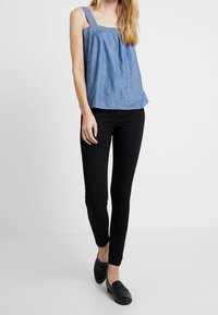 Niebieski bezrękawnik z chambray z szerokimi ramiączkami i marszczonym dekoltem, w zestawieniu z czarnymi dopasowanymi spodniami i czarnymi loafersami. Prosty design.