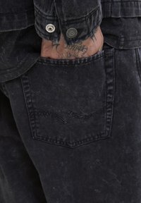 Sorte denim jeans med en falmet tekstur, der har en baglomme med en kontrasterende syet bølgedesign og metal knapdetaljer.