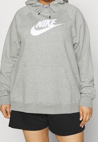 Grå huvtröja i mjukt tyg med en stor vit Nike-logotyp på framsidan och en känguruficka. Matchad med svarta shorts.