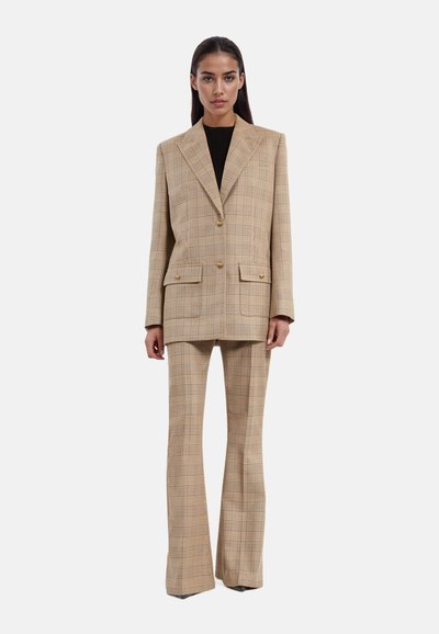 Blazer de doble botonadura de cuadros en color beige y pantalones acampanados de una tela texturizada, con botones dorados y dos bolsillos frontales.
