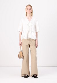 Top peplum bianco con dettagli ricamati e maniche a campana corte, abbinato a pantaloni beige a gamba larga e una borsa piccola. Indossate ballerine nere.