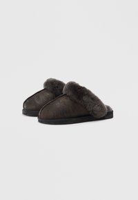 Brown suede slippers with a fluffy grey fur cuff, flat black sole, and a rounded toe design.
