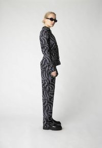 Schwarz-graues gemustertes zwei-teiliges Outfit mit langen Ärmeln, taillierter Passform und hochgeschnittenen Hosen, kombiniert mit schwarzen Plateaustiefeln.
