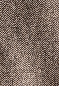 Gewebter Stoff mit einem Fischgrätenmuster in Braun- und Beigetönen, der eine grobe Textur und subtile Farbvariationen aufweist.