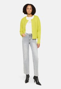 Limonkowo-zielony kardigan na guziki, noszony na białą koszulę. Dobranie do jasnoszarych dżinsów i czarnych botków z ostrym noskiem.