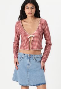 Rdeča gingham cropped majica z dolgimi rokavi, čipkastim robom in zavezovanjem. V kombinaciji z modrim denim A-linijskim krilom z žepoma.