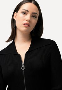Pull en tricot côtelé noir avec un grand col et un détail de fermeture éclair en argent. Caractérisé par une coupe ajustée et une texture lisse.