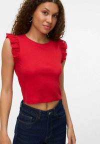 Rode crop top van ribstof, met kanten ruffles mouwen. Gepaard met donkerblauwe jeans, met een slim fit.