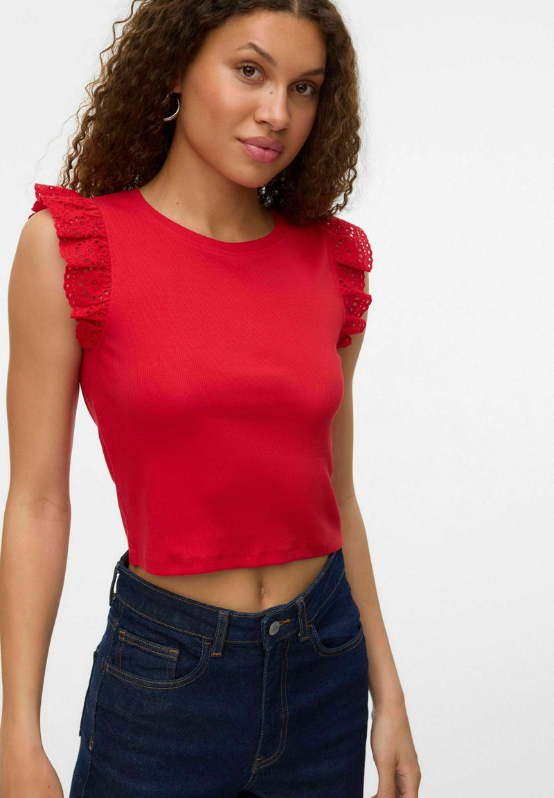 Rode crop top van ribstof, met kanten ruffles mouwen. Gepaard met donkerblauwe jeans, met een slim fit.