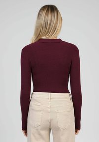Pull bordeaux côtelé avec un col, manches longues. Associé à un pantalon beige taille haute, avec poches arrière et tissu lisse.