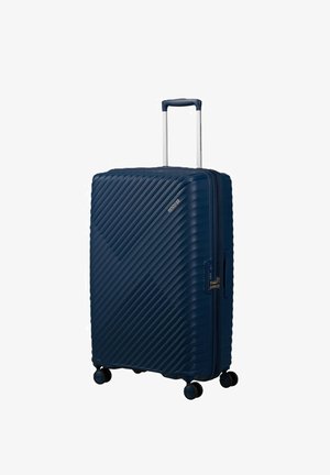 Valigia rigida blu navy con scanalature diagonali, manico telescopico, serratura laterale e quattro ruote girevoli multidirezionali.