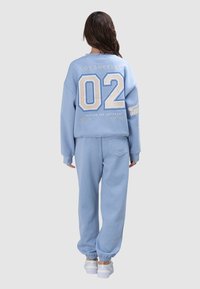 Hellblauer Pullover und passende Sweatpants. Der Pullover zeigt "LOS ANGELES" und eine große "02" in Cremefarbe. Weicher Stoff, lockere Passform, Bündchen an den Hosenbeinen.