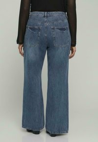 Jeans in denim blu a gamba larga con vita alta, dotati di due tasche posteriori e una delicata finitura sbiadita. Dettagli del cinturino e dell'orlo cuciti.
