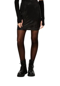 Schwarzer Pailletten-Minirock mit passgenauer Silhouette, kombiniert mit schwarzen opaken Strumpfhosen und klobigen schwarzen Schnürstiefeln. Die Textur wirkt glänzend.