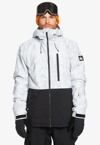 Weiße und schwarze Schneejacke mit Kamo-Muster, Frontreißverschluss, verstellbarer Kapuze und schwarzen Handschuhen. Verfügt über das Markenlogo auf dem Ärmel.