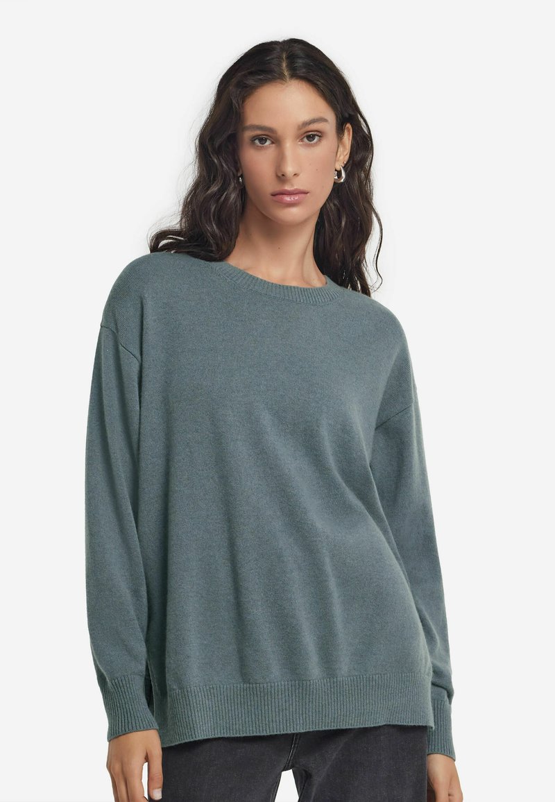 Ljusblå-grön oversized tröja med långa ärmar, ribbad halsringning och fåll. Mjuk textur och avslappnad passform, matchas med mörka jeans.