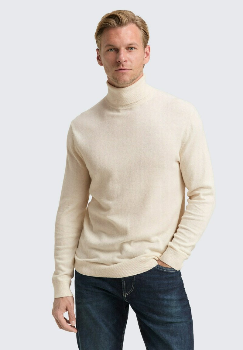 Lichtbeige coltrui gemaakt van zachte gebreide stof, met lange mouwen en geribbelde manchetten, gecombineerd met donkerblauwe jeans.
