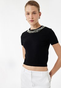 Sort kortærmet strikbluse med en tekstureret perleudsmykning omkring udskæringen. Tætsiddende design, cropped længde og ribbet kant.
