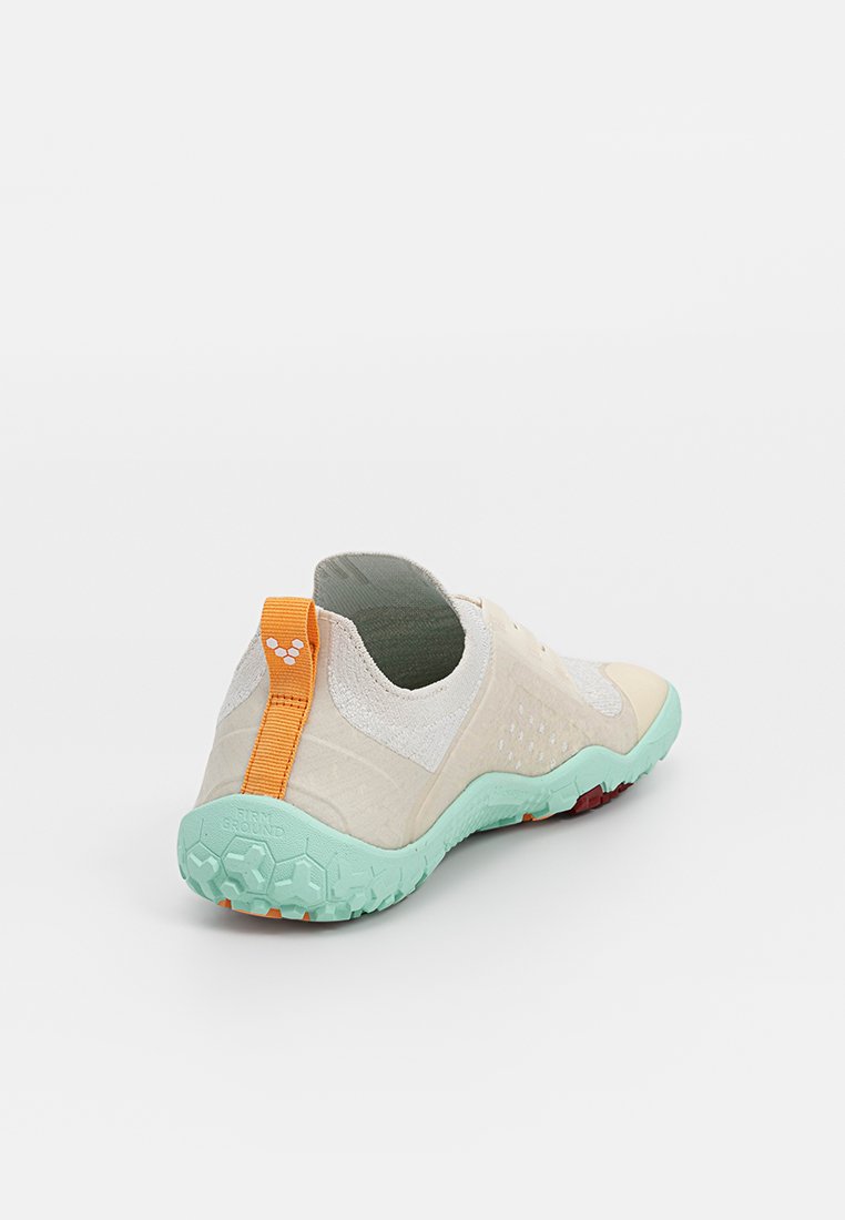 Zapatilla con parte superior de color crema, acentos texturizados y suela verde. Cuenta con una lengüeta de tira naranja y un diseño de perfil bajo para facilitar su uso.