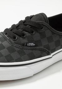 Czarno-szare w kratkę trampki Vans z czarnymi sznurowadłami i białą gumową podeszwą z czarnym paskiem, zbliżenie na bok i przód.