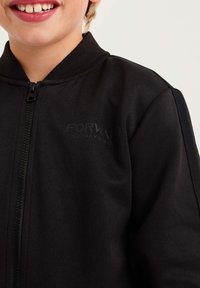 Czarna kurtka na zamek błyskawiczny z stójką, o teksturowanym wykończeniu oraz subtelnym nadrukiem logo z przodu. Posiada eleganckie boczne panele.