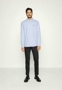Light blue button-up shirt with long sleeves, collar, and a chest pocket, paired with black slim-fit trousers and black shoes.