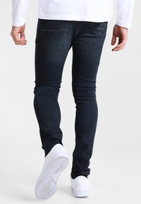 Tmavě modré slim fit džíny s hladkou strukturou, pěti kapsami a bílými teniskami, s jednoduchým vzorem a rovnými nohavicemi.
