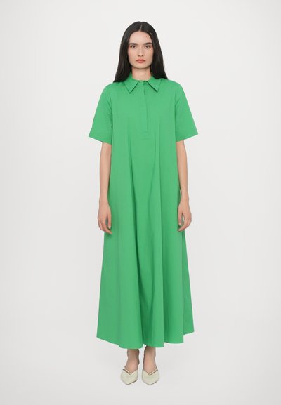 Abito di cotone verde con colletto, maniche corte e una silhouette ampia e fluida che arriva fino alle caviglie. Design semplice, texture liscia.