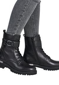 Bottines noires en cuir avec un devant à lacets, zip sur le côté et sangle ajustable. Elles sont dotées d'une semelle texturée et d'un accent en argent au niveau du talon.
