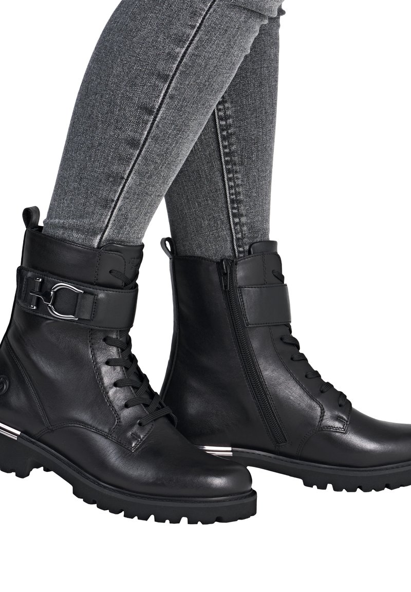 Bottines noires en cuir avec un devant à lacets, zip sur le côté et sangle ajustable. Elles sont dotées d'une semelle texturée et d'un accent en argent au niveau du talon.