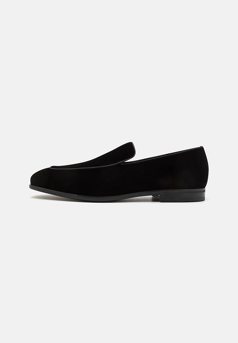 Black suede loafers featuring a low, textured heel and sleek, rounded toe. Minimalist design with no additional embellishments.