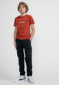 Rode katoenen T-shirt met 'Petrol Industries' print, gecombineerd met zwarte cargobroeken en witte sneakers. Casual urban outfit, met elastische boorden.