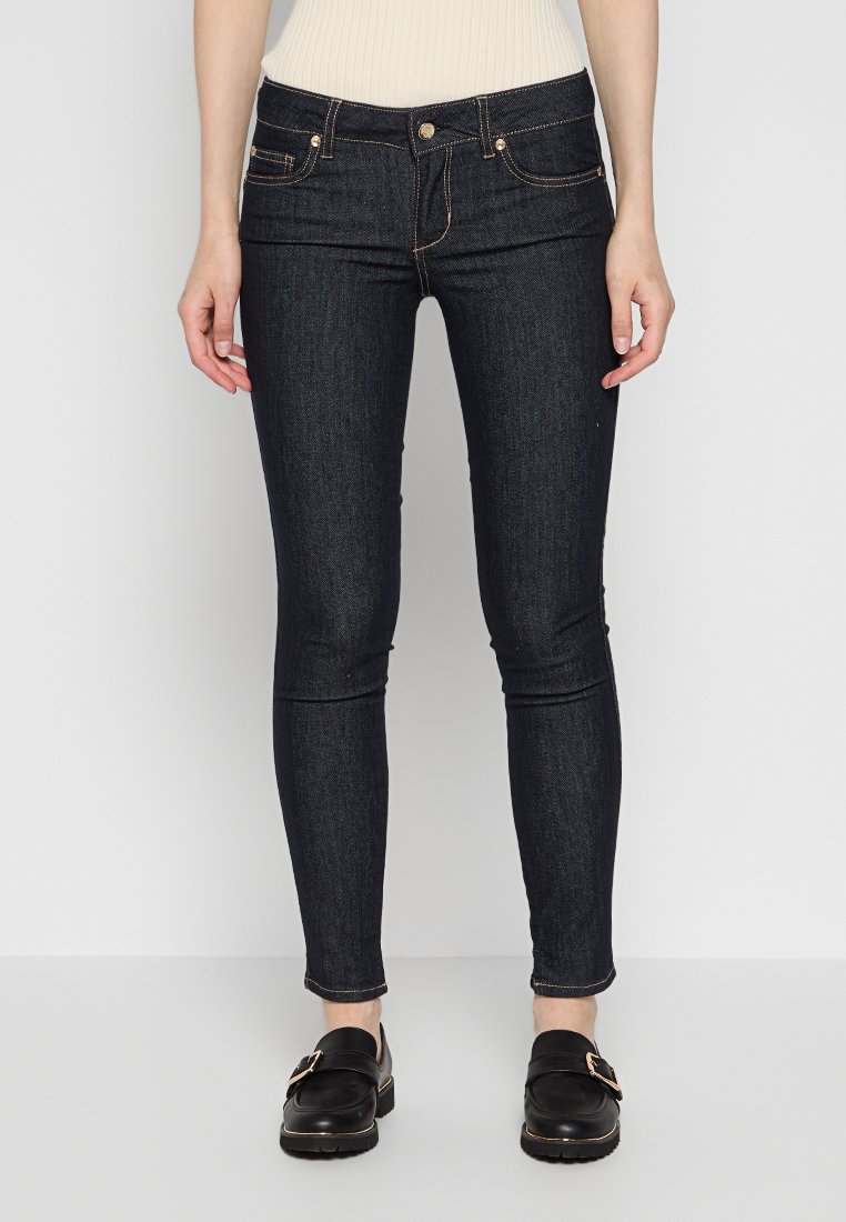 Skinny jeans in donkere denim, met vijf zakken, gouden stiksels en een knoopsluiting. Gepaard met zwarte loafers.