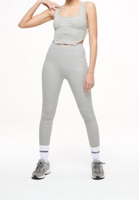 Ljusgrå, ribbad crop top med fyrkantig halsringning och logotyp; matchande ribbade högmidjade leggings. Grå sportskor med vita strumpor.