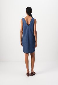 Vestido de ganga com um decote profundo nas costas e design sem mangas, apresentando um corte reto e bainha crua. O tecido tem um lavagem média e textura suave.