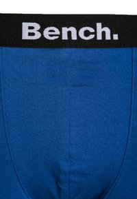 Kék fehérnemű bordázott felülettel, fekete derékszíjjal, amelyen fehér betűkkel szerepel a "Bench." márkanevé.