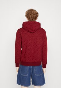 Sudadera burdeos con una textura estampada, que presenta una capucha con cordón y puños de canalé, combinada con shorts de mezclilla azules.