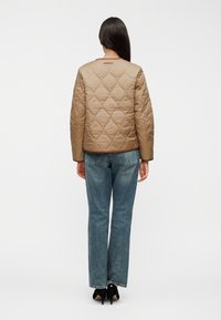 Ταμπά καπιτονέ μπουφάν με μοτίβο διαμαντιού, στρογγυλή λαιμόκοψη, μακριά μανίκια και ελαφρύ υλικό. Φορεμένο πάνω από μπλε τζιν παντελόνια με ίσιο πόδι.