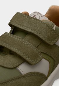 Πράσινο και μπεζ αθλητικό παπούτσι με δύο μεγάλους ιμάντες με αυτοκόλλητο και ορατή ετικέτα μάρκας στη γλώσσα.