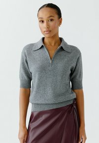 Grijze gebreide trui met een ritskraag en korte mouwen, gecombineerd met een bordeaux leren rok met een zijstrikdetail.