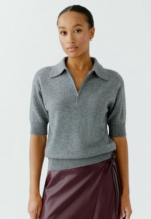 Grijze gebreide trui met een ritskraag en korte mouwen, gecombineerd met een bordeaux leren rok met een zijstrikdetail.