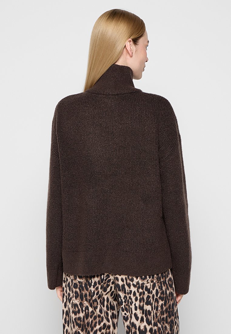 Brauner gestrickter Pullover mit hohem Kragen, lockerer Passform und gerippter Textur. Getragen mit gemusterten Leopardenprint-Hosen. Rückenansicht.