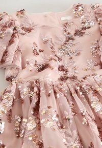 Pink kjole med blomster broderet i palietter, bølgede ærmer og en flagrende nederdel. Lavet af tyl og foret med et blødt stof.