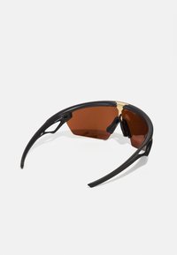 Schwarze Sportsonnenbrille mit braun getönten Gläsern, einem goldenen Akzent an der Brücke und strukturierten schwarzen Ohrstützen für Stabilität.
