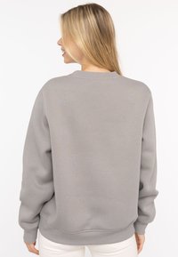 Grauer Pullover mit Rundhalsausschnitt, langen Ärmeln und gerippten Bündchen. Einfaches Design, aus weichem Stoff mit glatter Textur.