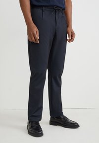 Pantalon stretch bleu marine à tissage texturé, doté d'une taille à cordon de serrage et d'une coupe droite, associé à des chaussures en cuir noir à enfiler.