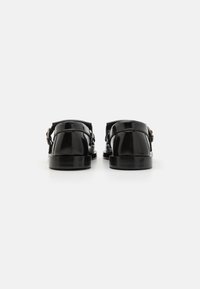 Schwarze Lacklederschuhe mit einer hinteren Schnalle, flacher Sohle und glatter Textur; zeichnen sich durch ein minimalistisches Design ohne sichtbare Muster aus.