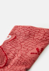 Röd mönstrad strumpa med en texturerad, fjäll-liknande design. Tillverkad av mjukt material, med en elastisk topp för passform och komfort.